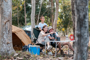 A cheerful family camping in the forest, sitting by a tent with a picnic table, enjoying nature and each other's company.