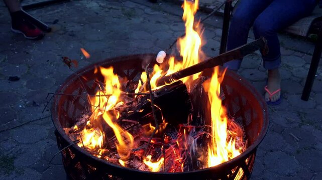 Friends gather around glowing campfire, roasting marshmallows while enjoying summer evening outdoors.