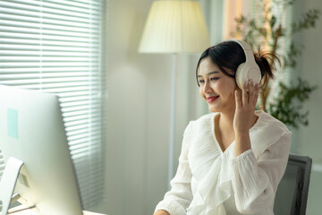 A woman wearing headphones is sitting at a desk in front of a computer monitor