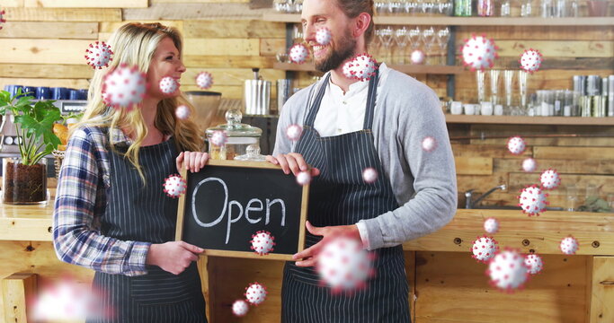 Cafe owners smiling, holding open sign, surrounded by illustrated virus particles