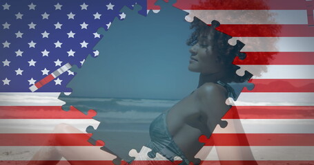 Image of american flag waving with jigsaw puzzles revealing biracial woman on beach
