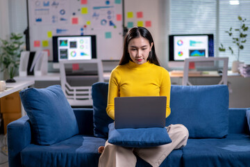A woman is sitting on a blue couch and using a laptop