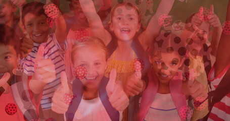 Digital composite image of covid-19 cells moving against group of kids showing thumbs up at school