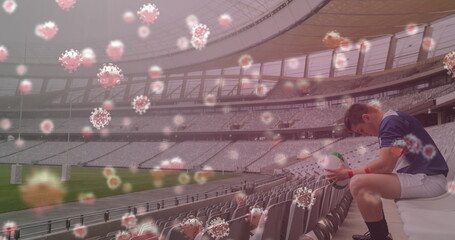 Image of 3d coronavirus cells floating over rugby player holding rugby ball on empty stadium