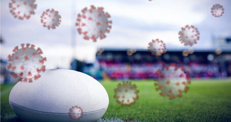 Image of coronavirus cells floating over empty stadium and rugby ball