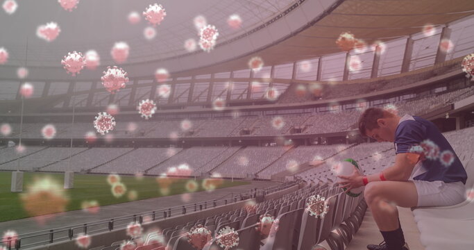 Image of 3d coronavirus cells floating over rugby player holding rugby ball on empty stadium