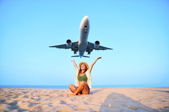 Happy satisfied smiling cheerful joyful traveler girl with open arms watching airplane flying overhead