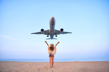 Happy free traveler girl with open arms watching airplane flying overhead, ready to traveling