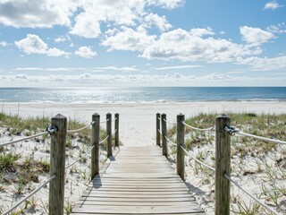 A wooden boardwalk leads to a serene beach, sunlight cast on the sand dunes, full of natural beauty.