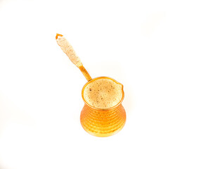 Turkish coffee pot (cezve) with foamy freshly brewed organic coffee isolated against a white background