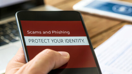 A hand holding a smartphone displaying a warning about scams and phishing, emphasizing the importance of protecting personal identity.