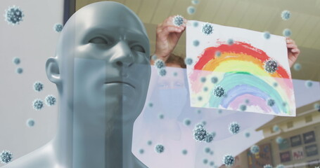 Image of covid 19 cells over model head with person in face mask holding rainbow drawing