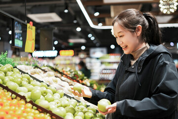 Woman Joyfully Selecting Fresh Green Apples in a Modern Grocery Store