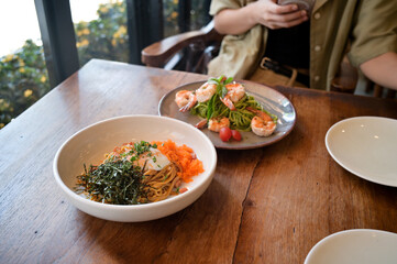 delightful serving of spaghetti topped with roasted seaweed, eggs and roe is paired with plate of pesto spaghetti garnished with shrimp and cherry tomatoes, creating flavorful meal