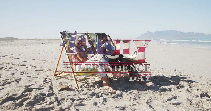 Independence day text against senior caucasian couple sitting on deck chairs at beach