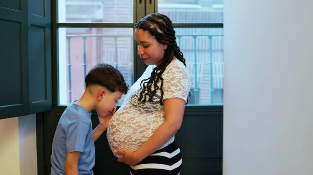 Latin kid whispering to his pregnant mom's belly at home