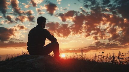 Silhouette of a man sitting on a cliff overlooking a beautiful sunset.