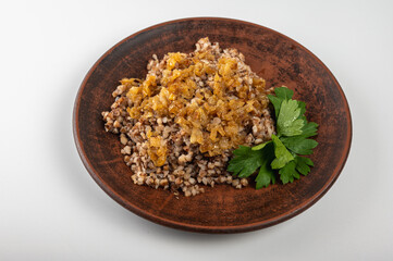 Traditional buckwheat porridge with caramelized onions on a rustic plate. A hearty, nutritious and aromatic dish, popular in Eastern European cuisine, on a clay plate, on a white background