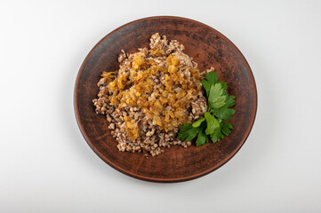 Traditional buckwheat porridge with caramelized onions on a rustic plate. A hearty, nutritious and aromatic dish, popular in Eastern European cuisine, on a clay plate, on a white background