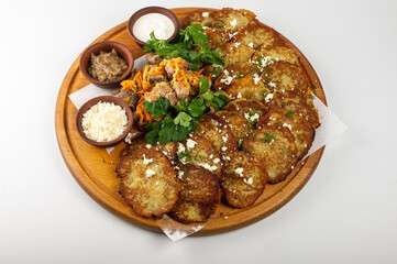 Traditional Belarusian or Ukrainian potato pancakes with fried meat, sauted vegetables, sour cream, cheese, mushroom sauce, and fresh herbs on a wooden platter