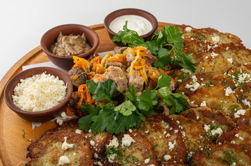 Traditional Belarusian or Ukrainian dumplings with fried meat, sautéed vegetables, sour cream, cheese, mushroom sauce and herbs on a wooden platter