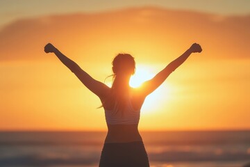 Fototapeta premium Woman with arms raised facing golden sunset silhouette at the beach. It can portray success, freedom, health, wellbeing, and spiritual concept.