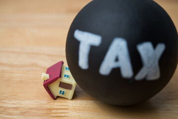 Heavy tax crash the house model on wooden table background. House building and land tax, property...
