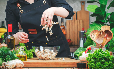 Cook pours oyster mushrooms in glass bowl.  Cozy kitchen with wooden table, kitchenware,...