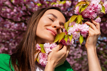 Fototapeta premium Happy smiling woman enjoys the softness of cherry tree flowers