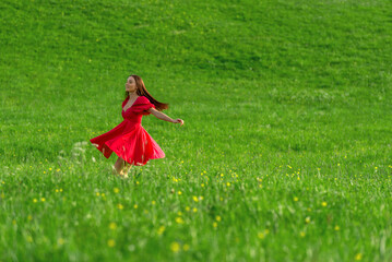 Happy woman in pink dress spins in the green grass at sunset