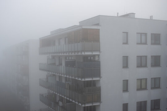 A thick fog blankets the city as seen from the balcony of an apartment building on a foggy early spring morning, with buildings barely visible in the mist.