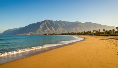 Golden sandy beach and clear blue sea with a backdrop of mountains,