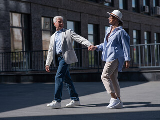 Stylish mature couple. Gray-haired man and woman holding hands while walking around the city. 