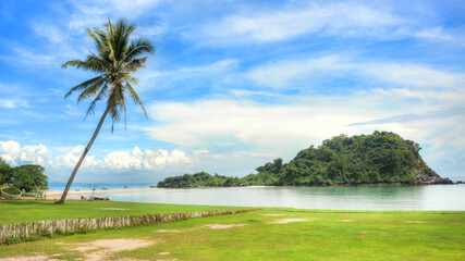 Summer beach with coconut palm trees and a tranquil island in background