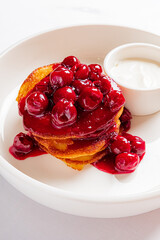 Fluffy pancakes with cherry sauce and a side of yogurt
