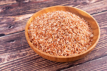 Raw brown whole rice in a bowl over wooden table.