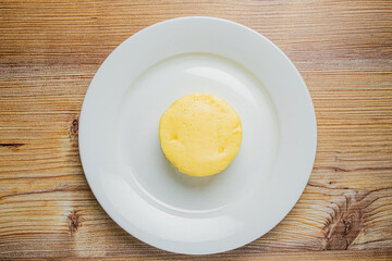 A round yellow dessert on a plain white plate invites indulgence during a cozy meal