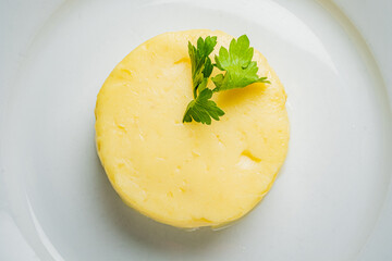 A smooth dollop of butter topped with fresh herbs sits elegantly on a white dish