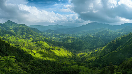 Naklejka premium Breathtaking Panoramic View of Lush Green Mountains Under a Dramatic Sky with Clouds and Sunlight Casting Shadows Over the Verdant Landscape