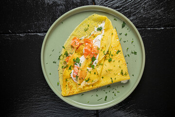 A delicious crepe garnished with ripe tomatoes and fresh herbs lies elegantly on a modern plate