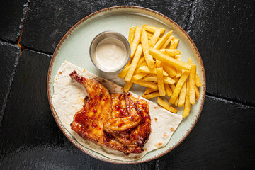 Delicious grilled chicken accompanied by golden fries and a savory dipping sauce on a rustic plate