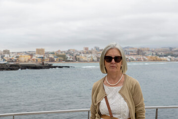 Fototapeta premium Elderly Woman Wearing Sunglasses with Scenic Coastal View in the Background