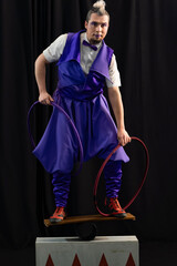 Male artist wearing purple costume balancing on seesaw while holding hoops, performing in circus show