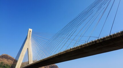 Obraz premium Dynamic low-angle photo of a suspension bridge, cables extending gracefully into a cloudless blue sky, highlighting engineering innovation. 