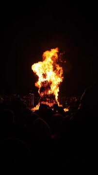 Burning of large straw effigy Winter on square on street during Maslenitsa holiday. Pagan ritual. Lots of people spectating around. Festivities festival outdoors. Vertical