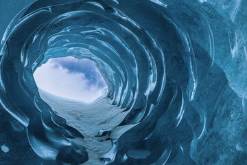 An ice tunnel to the blue sky in an ice cave in the Morteratsch Glacier, Grions, Switzerland (March...