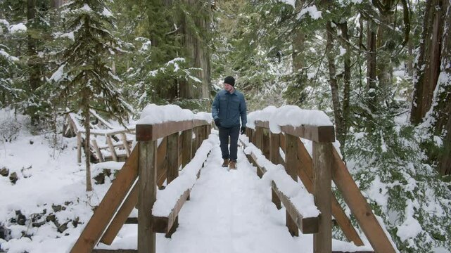 Caucasian Man Hiking Over Snow Covered Wood Bridge in Washington Forest