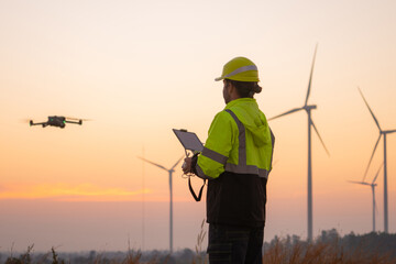 Engineers male flying drone surveying and checking wind turbines from the high angle view of the field during beautiful sunset. using drone technology for work.