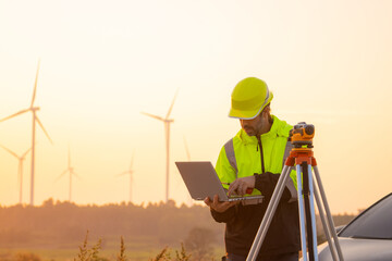 Engineer working on laptop in front of wind turbines for checking wind turbines of the field during beautiful sunset. Alternative energy concept.