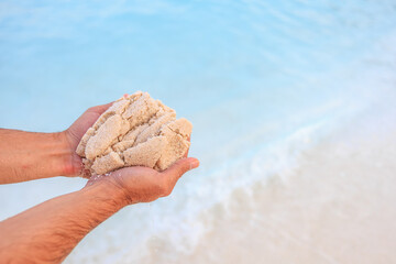 A man is holding a handful of sand on a beach